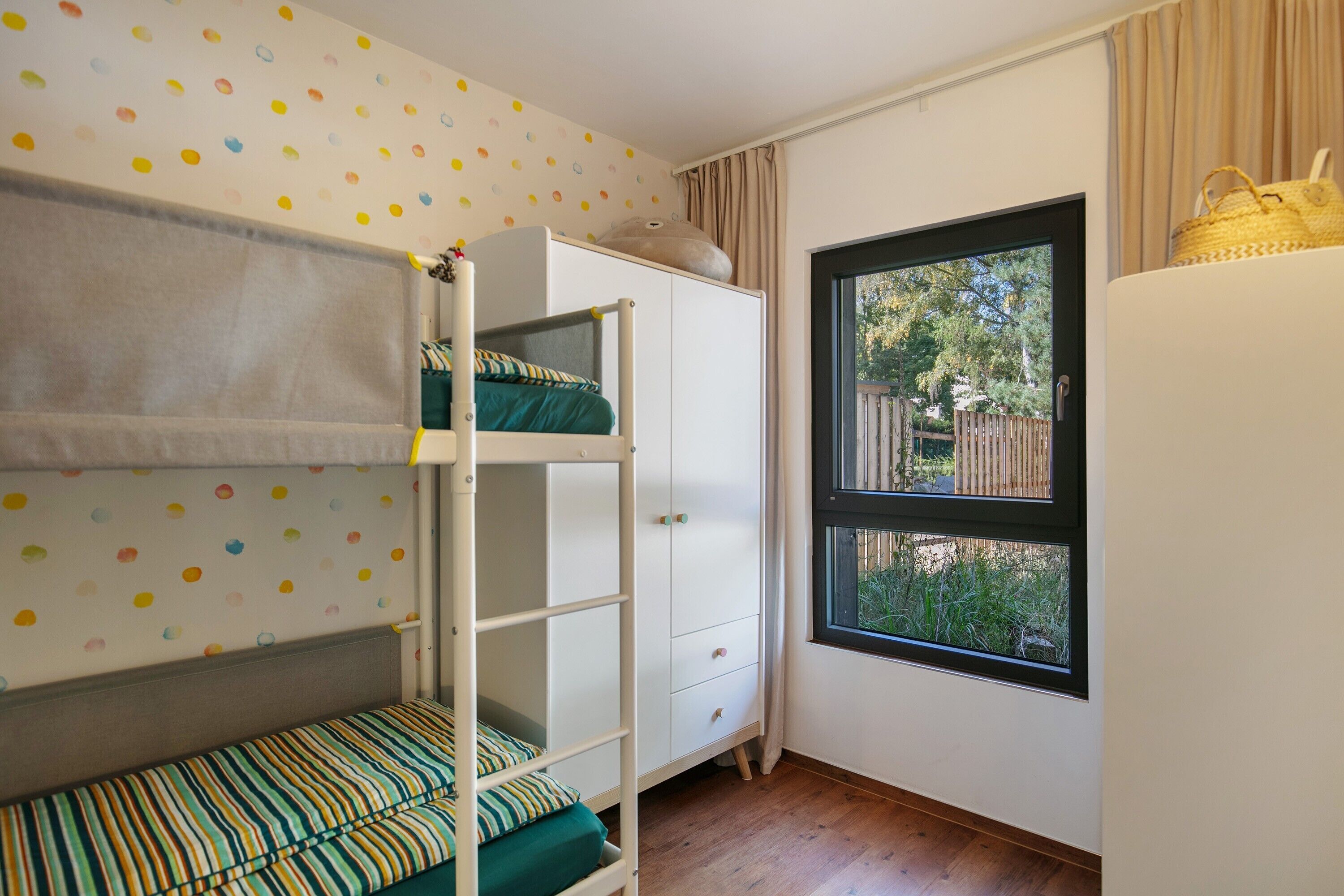Ein Zimmer mit Etagenbetten, einem Fenster mit Blick auf Grünflächen und einem weißen Schrank.