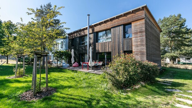 Un bâtiment moderne à deux étages, doté d’une façade en bois, de grandes fenêtres et d’un jardin bien entretenu agrémenté de mobilier d’extérieur.