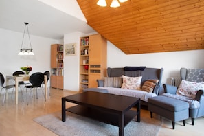 A modern living room with a wooden ceiling, a sofa, a coffee table, a bookshelf, and a dining area.