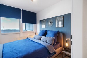Une chambre à coucher avec un lit, une table de chevet, une lampe et une vue sur la ville par la fenêtre.