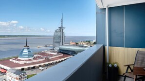 A balcony with a view of a waterfront, a modern building with a spire, and a distinctive blue dome structure. - Apartment 'Clara' with Sea View, Balcony and Wi-Fi (Bremerhaven)