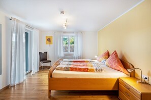 Une chambre à coucher avec un lit, une chaise, une table de chevet et une fenêtre avec des rideaux.
