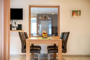Un coin repas avec une table en bois et des chaises noires, un téléviseur à écran plat fixé au mur et un tableau encadré.