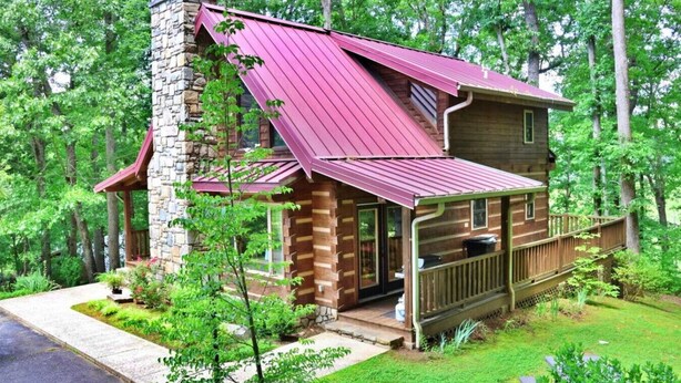 Eine Blockhütte mit einem Steinkamin, einem roten Metalldach und einer Holzterrasse.
