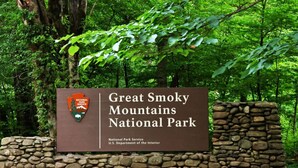 A sign for Great Smoky Mountains National Park with a stone wall and lush greenery in the background.
