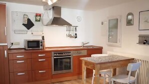 Una cocina compacta con armarios de madera, un microondas, un horno, un lavabo y una mesa de comedor con sillas.