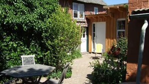 Un patio con una mesa y sillas, una casa de ladrillo al fondo y un área ajardinada.
