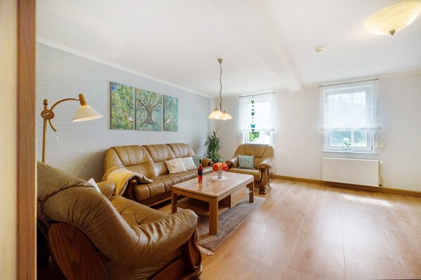 A living room with a sofa, coffee table, and two chairs, a floor lamp, and a painting on the wall.