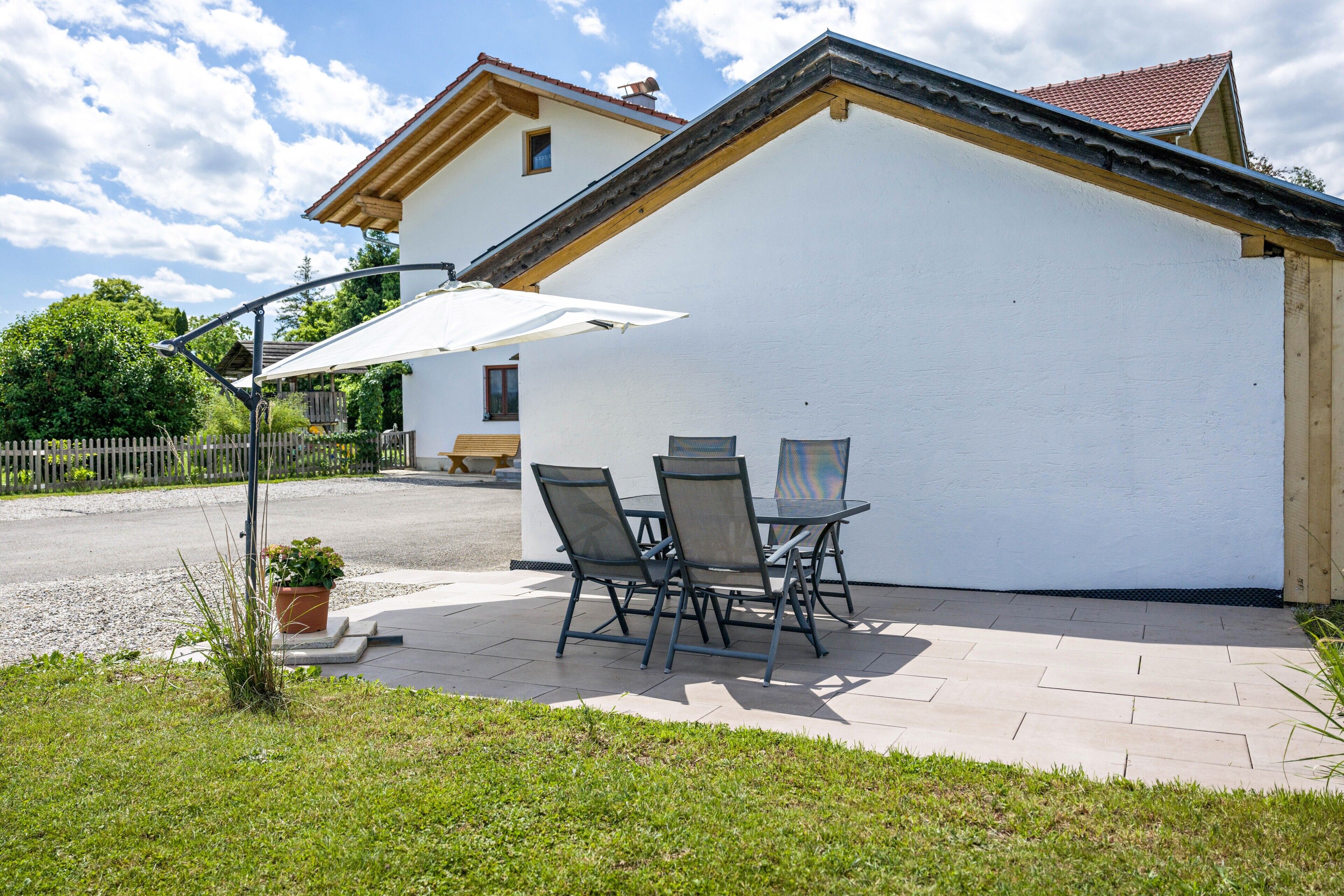 A patio with a table and chairs, a white building, and a street in the background.
