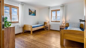 Una habitación con dos camas de madera, un radiador, una ventana con cortinas, una mesita de noche con lámpara y un cuadro en la pared.