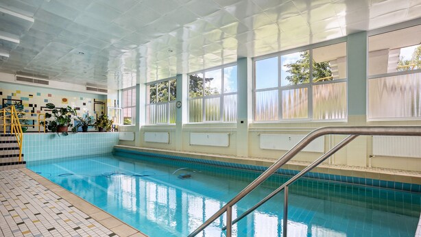 Una piscina interior con paredes de vidrio transparente, suelo de baldosas y una escalera.