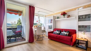 Una sala de estar moderna con un sofá rojo, un comedor y un ventanal corredero que da a un espacio exterior.