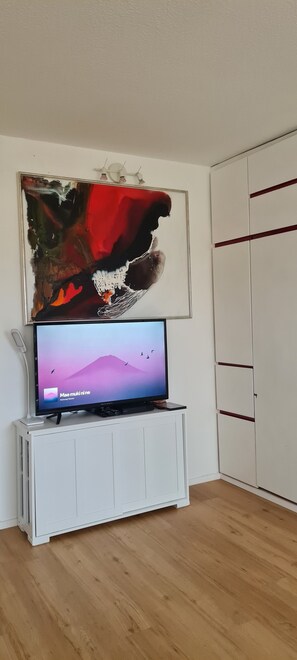 A room with a flat-screen TV on a white cabinet, a large abstract painting above it, and a wardrobe with horizontal stripes.