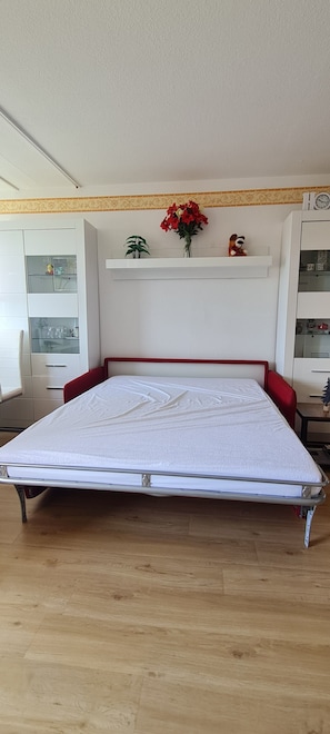 Ein Zimmer mit einem Bett, Holzboden, einer weißen Decke und einem Regal mit Dekoration.