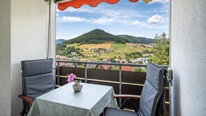 Un balcón con mesa y sillas, vistas a un paisaje montañoso y cielo despejado.