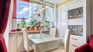 Un comedor con una mesa dispuesta para dos, una ventana con vistas a zonas verdes y un aparador con puertas de cristal.