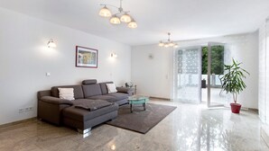 Una sala de estar moderna con un sofá, una mesa de centro de vidrio, una planta en maceta y un amplio ventanal corredizo que da a un área exterior.