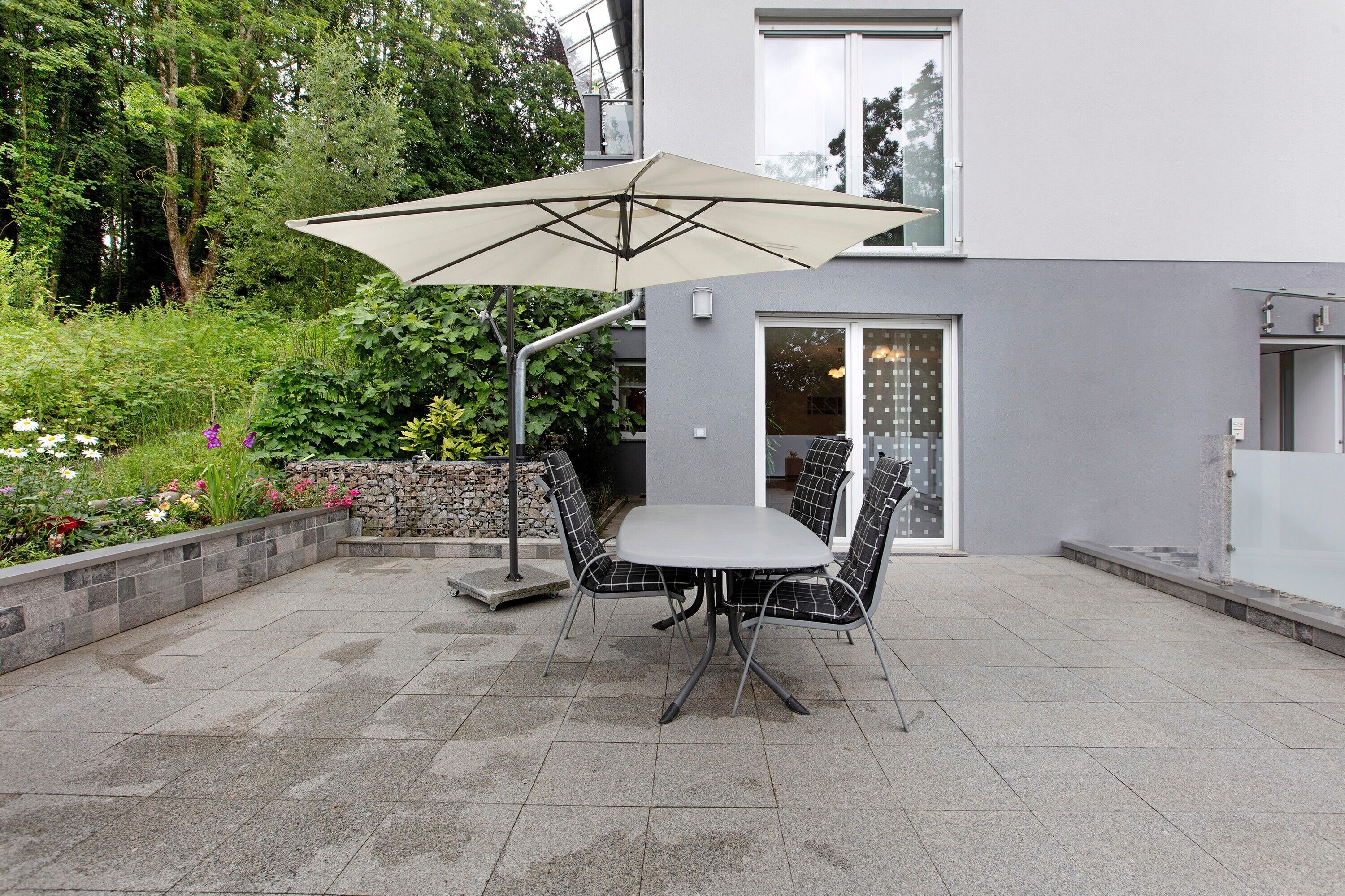 En terrasse med et bord, stole, en parasol og en stenvæg med planter.
