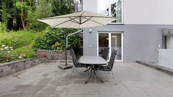 En terrasse med et bord, stole, en parasol og en stenvæg med planter.
