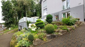 Un edificio residencial con un camino de entrada pavimentado, un jardín con diversas plantas y flores, y un buzón.