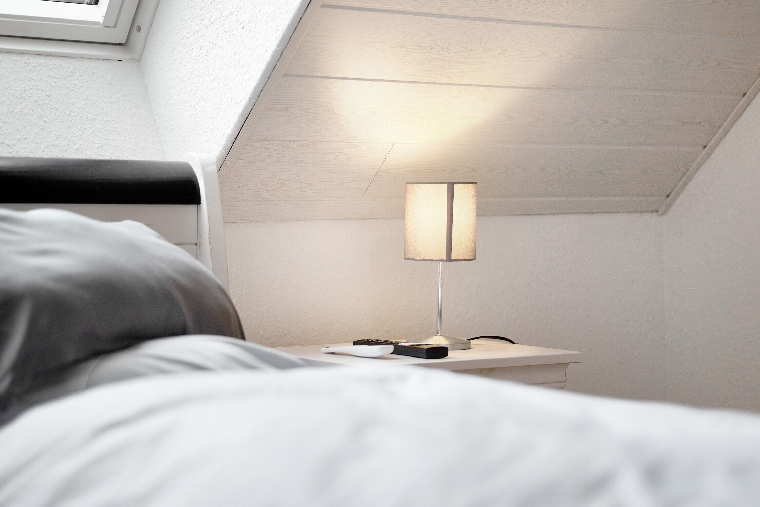 A bedroom with a bed, a bedside table with a lamp, and a window.