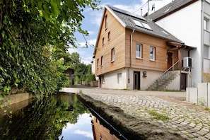 Une maison en bois avec une cour dallée et un étroit canal d’eau.