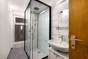 Ein modernes Badezimmer mit einer glĂ€sernen Dusche, einem weiĂen Waschbecken und einer HolztĂŒr.