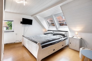Une chambre à coucher avec un lit, un téléviseur fixé au mur, une fenêtre et une table de chevet avec une lampe.