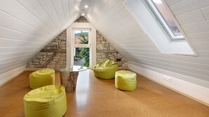 Una habitación con techo inclinado, pared de piedra, puerta de cristal y sillones orejeros verdes.