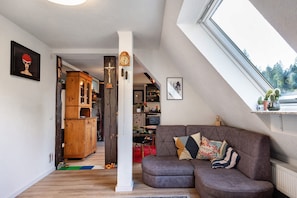 A loft-style living space with a wooden cabinet, a brown leather sofa, a dining area, and a view through a skylight.