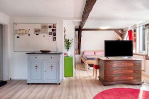 A room with a whiteboard, a wooden bed, a TV on a dresser, and a red rug.