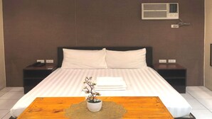 Hotelkamer met een bed, nachtkastjes, een airconditioner en een houten tafel met een plant in een pot.