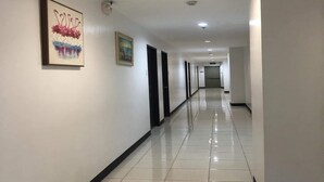 Een lange, goed verlichte gang met witte muren en een betegelde vloer, met twee ingelijste kunstwerken aan de linker muur.