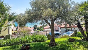 A residential area with a large tree, green grass, and a view of houses and a body of water in the background.
