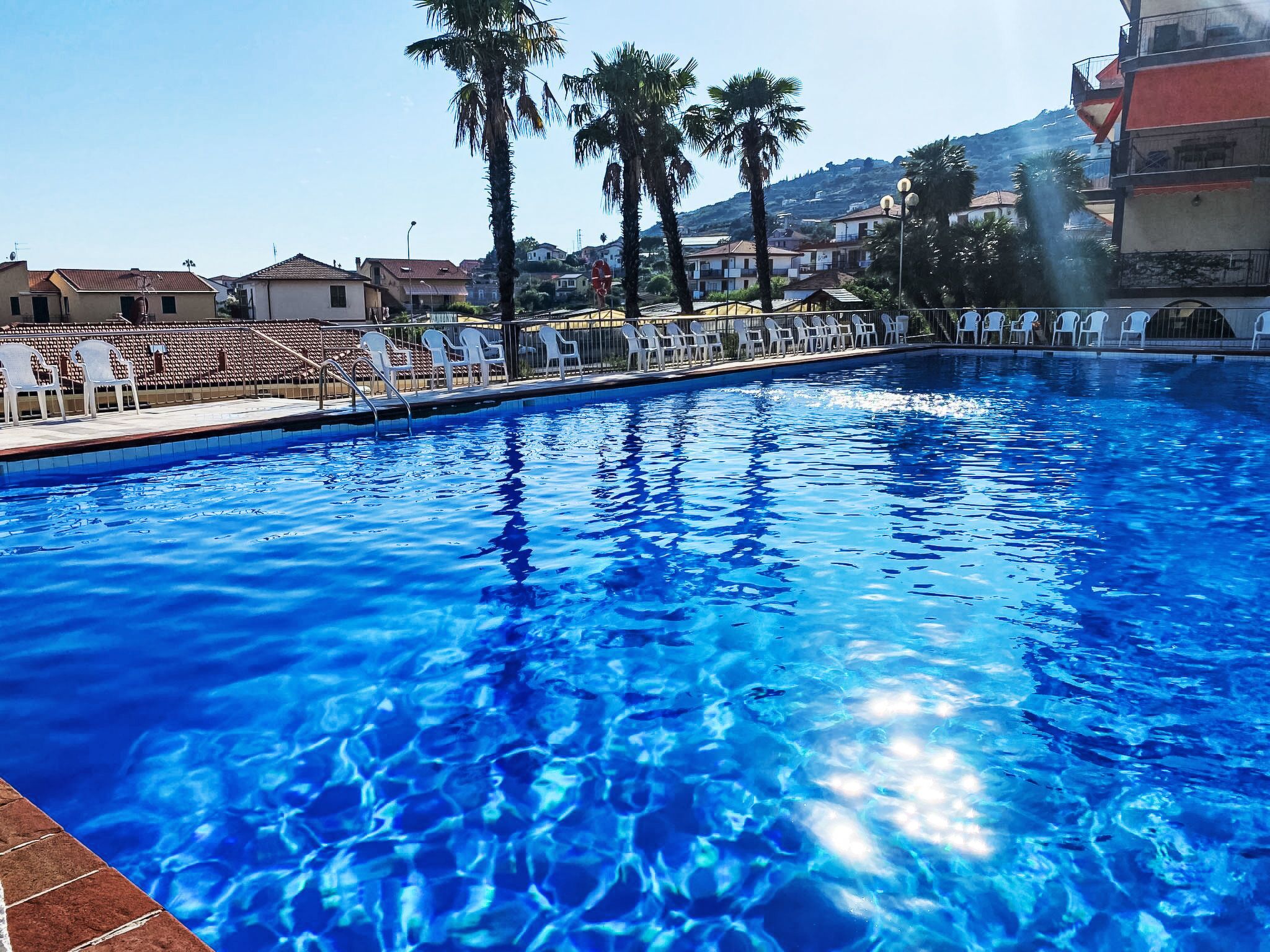 Ein Schwimmbecken mit klarem, blauem Wasser, umgeben von weißen Liegestühlen und Palmen.