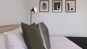 A neatly made bed with white and green pillows, a black and white patterned pillow, and a black floor lamp. There are three framed abstract artworks on the wall. - Phaedrus Living : Limassol Pyrgos Seaside Flat (Pyrgos)