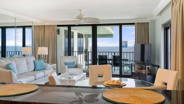 A spacious living room with a large window, a ceiling fan, and a dining area with a table and chairs. - Watercrest 1710 - Sleeps 8 (Panama City Beach)