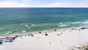 A beach with white sand, clear blue water, and several beach umbrellas. - Watercrest 1710 - Sleeps 8 (Panama City Beach)