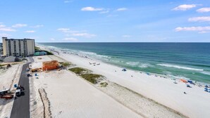 Una playa con una carretera que recorre la costa en paralelo, un edificio grande a la izquierda y el océano al fondo.