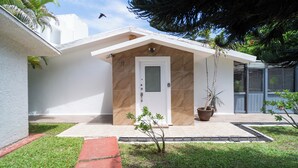 A modern house with a white exterior, a beige door, and a small garden area with a palm tree and a potted plant. - Charming 3BR House, Close To The Beach (Cancún)