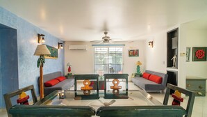 A living room with a glass-top dining table, two wooden chairs, a grey sofa, and a ceiling fan. - Charming 3BR House, Close To The Beach (Cancún)