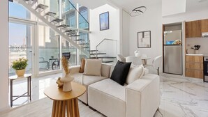 Ein modernes Wohnzimmer mit einem weißen Sofa, einem Holztisch und Blick auf eine Stadtlandschaft durch große Fenster.