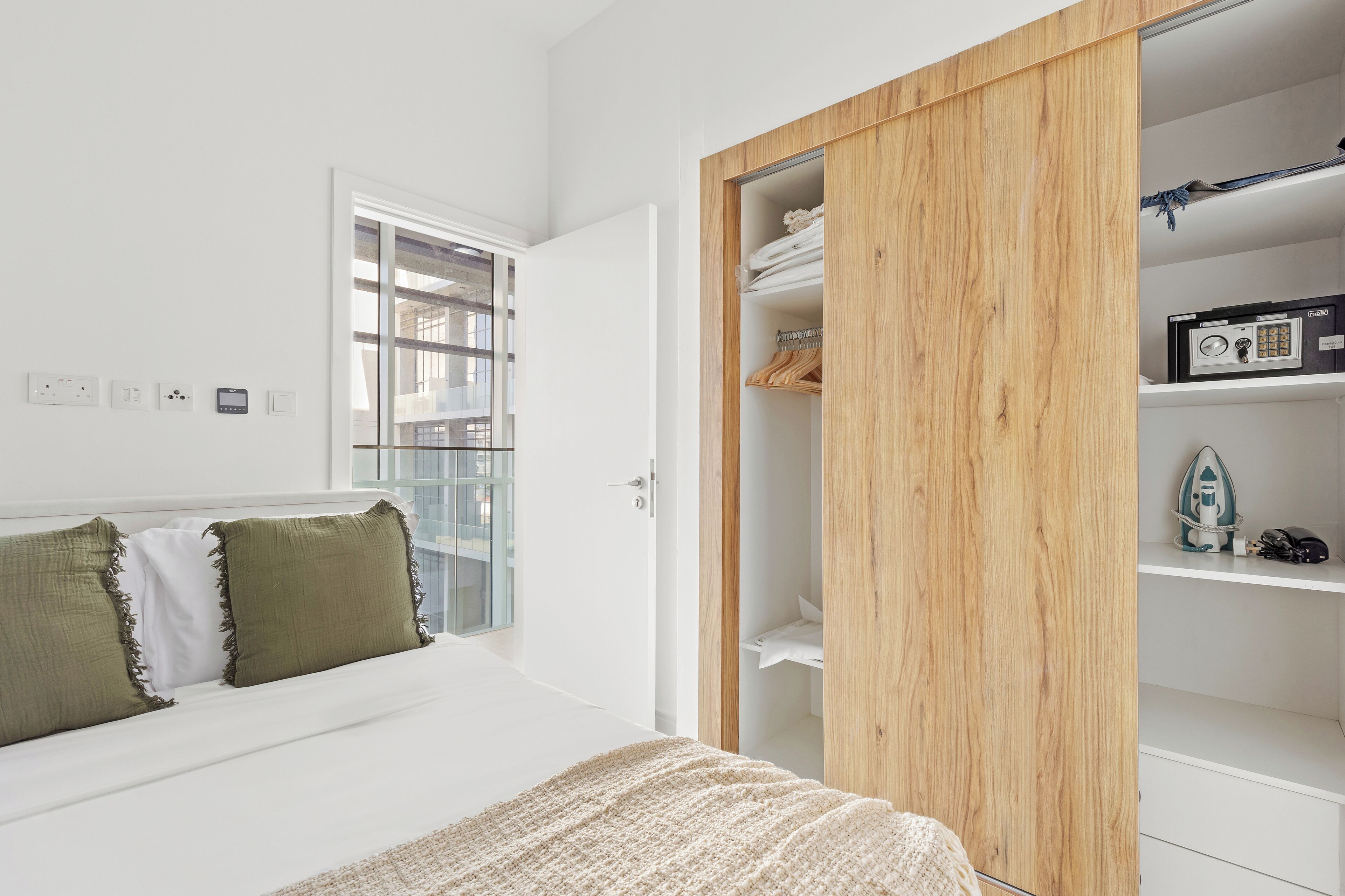 A bedroom with a bed, a wooden wardrobe, and a window.