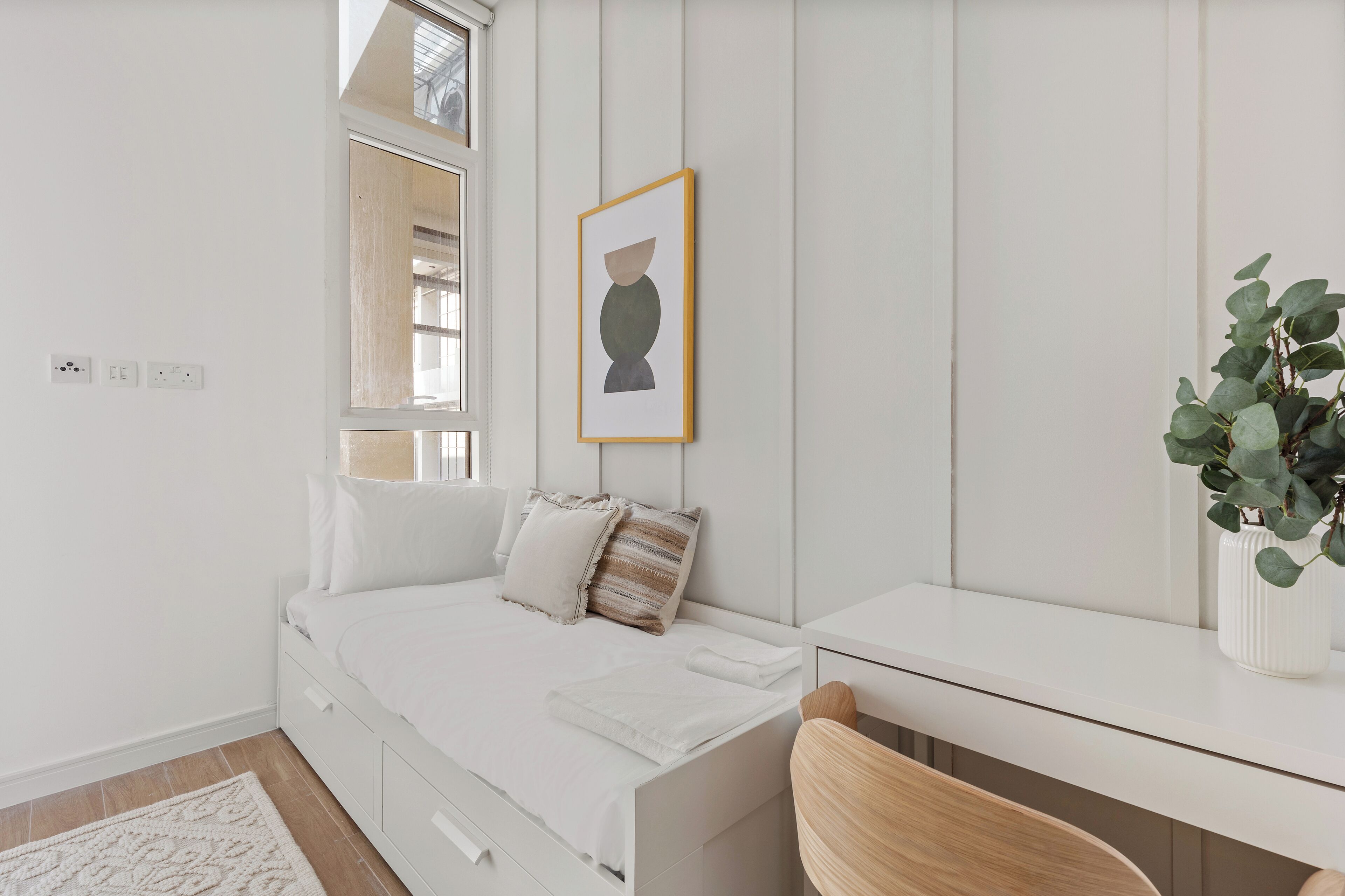 A minimalist bedroom with a bed, bedside table, and a potted plant.