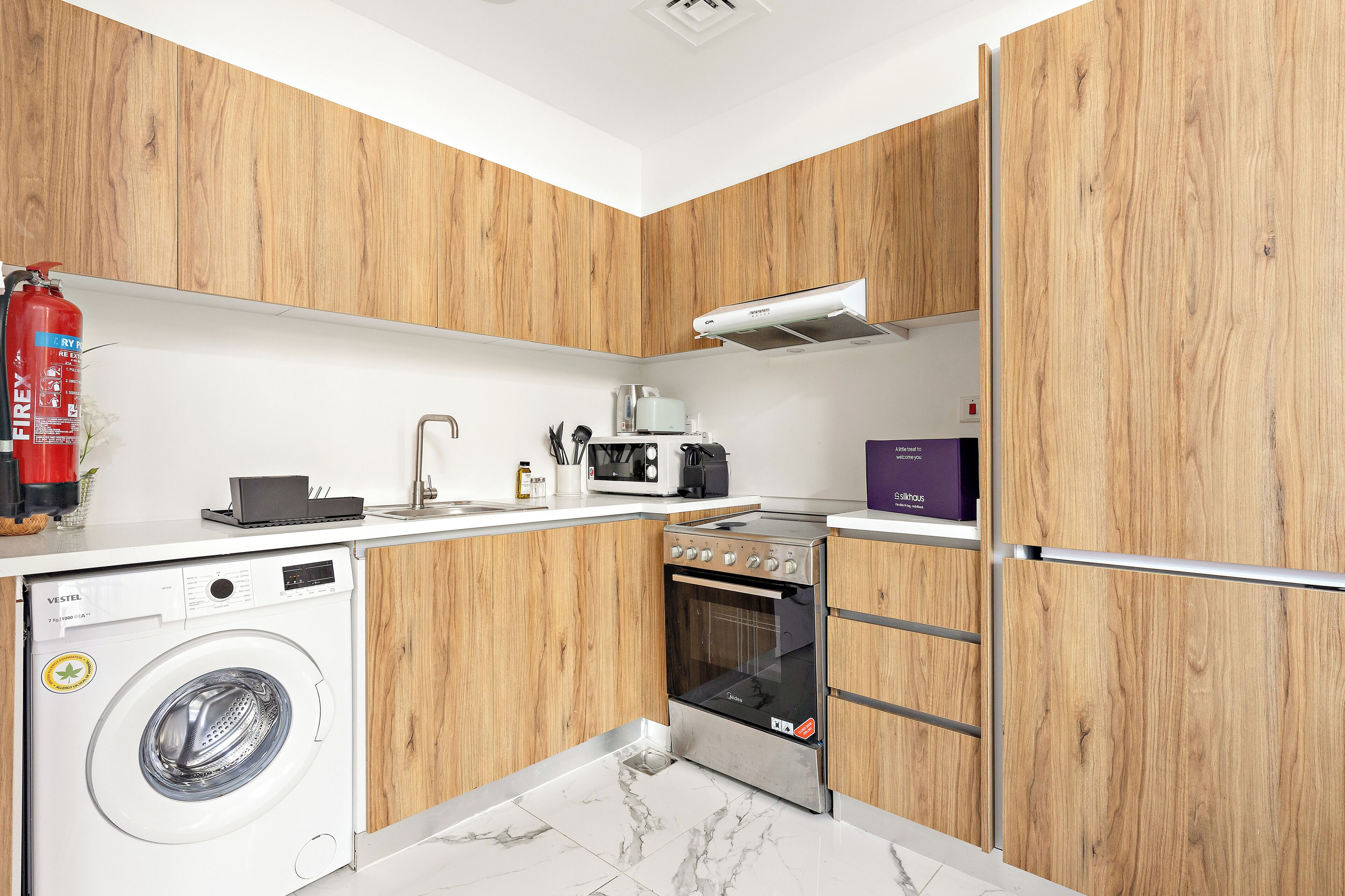 A compact kitchen with wooden cabinets, a washing machine, a microwave, and a stove.
