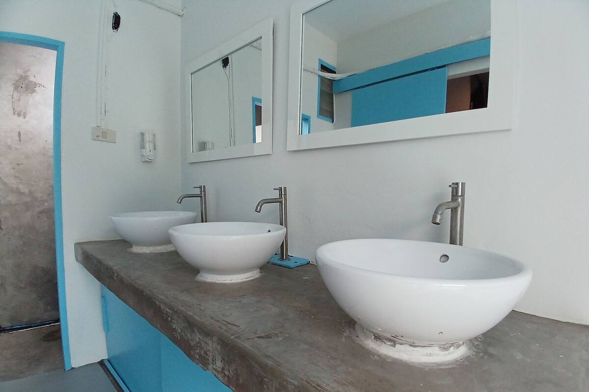 A bathroom with three white sinks on a grey countertop, a mirror above the sinks, and a blue accent wall.