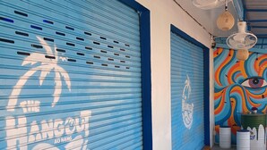 A hallway with closed blue shutters, a mural with a palm tree and a temple, and a ceiling fan. - The Hangout Ao Nang (Krabi)