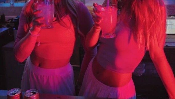 Two people sitting at a bar with drinks, a table with cans, and a red-lit ceiling. - The Hangout Ao Nang (Krabi)