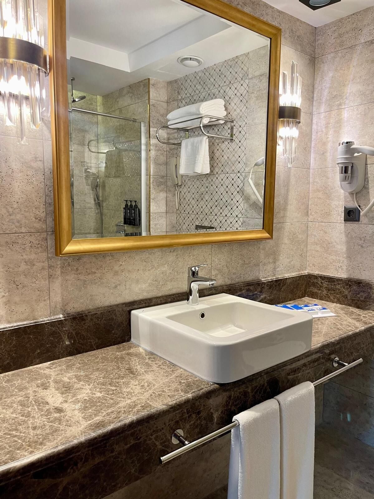 Un baño con un espejo grande, un lavabo, un perchero para toallas y una zona de ducha.