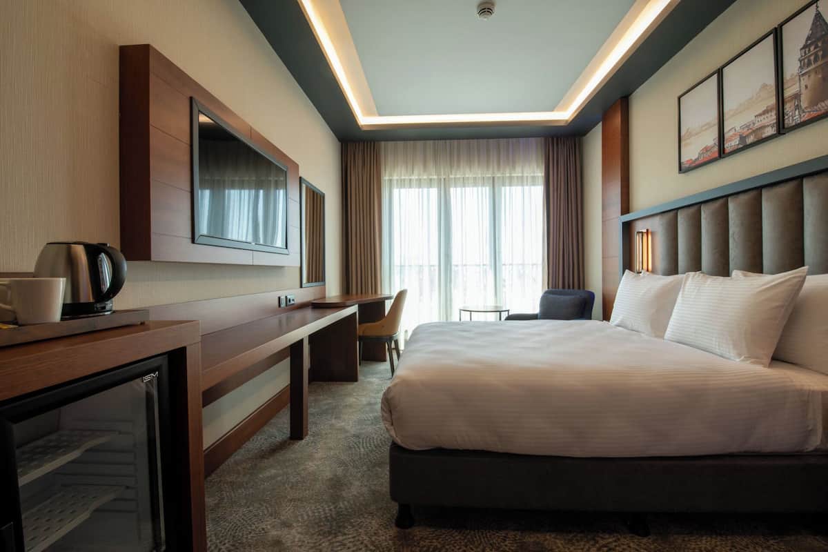 A hotel room with a bed, a desk, a chair, a television, and a coffee maker.